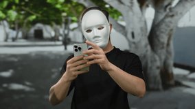 Young man with mask using smartphone on city street, surrounded by trees, creating a mysterious outdoor scene. - Powered by Shutterstock - Get 15% off with code: PIKWIZARD15