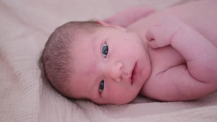 Newborn baby lying on soft blanket and looking directly at camera