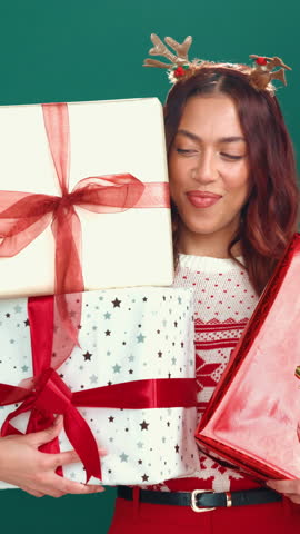 Christmas, face and happy woman with gift box in studio, dancing and excited for festive shopping. Holiday season, person laugh or present for sale announcement, deal and discount on green background