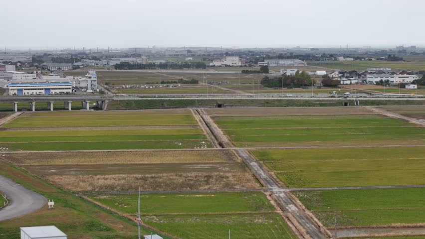 A large field with a few buildings in the background. The sky is cloudy and the grass is green