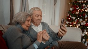 70-years-old spouses chatting online by video call in smartphone from home. Grandparents celebrating fabulous winter holidays, Christmas and new year vacation, cozy home interior with Christmas tree - Powered by Shutterstock - Get 15% off with code: PIKWIZARD15
