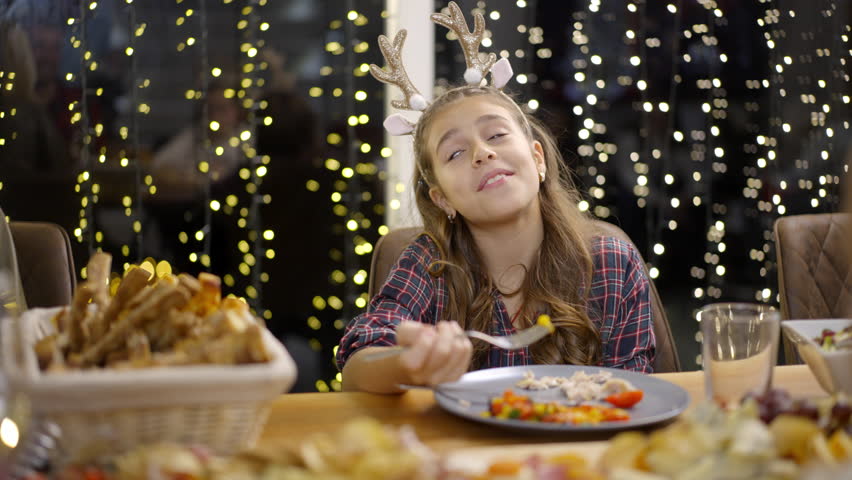A young girl smiles while eating a meal at a table decorated for a holiday celebration