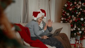 Christmas and New year, elderly spouses in cozy interior, video call by laptop. Beautiful Xmas decoration in living room, distant communication with family and friends, funny Santa hats and smiles - Powered by Shutterstock - Get 15% off with code: PIKWIZARD15