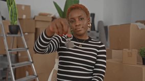 New woman holds house key up in building surrounded by moving boxes and houseplants; homeownership pride. - Powered by Shutterstock - Get 15% off with code: PIKWIZARD15