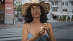 Woman in blue swimsuit applying deodorant on city street under sun hat during daytime. - Powered by Shutterstock - Get 15% off with code: PIKWIZARD15