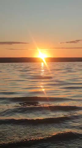 A serene sunset over a calm lake, with golden and orange hues reflecting on the water.