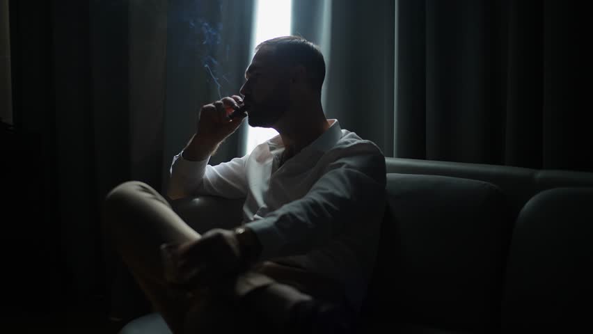 Elegant man smoking cigar and holding glass of whiskey in dark interior, stylish masculine portrait with soft light and smoke, concept of luxury lifestyle, relaxation and sophistication