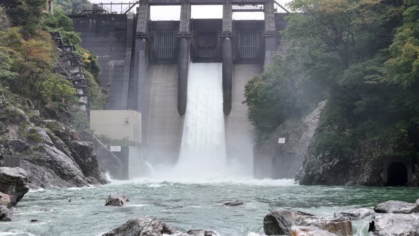 A large waterfall is flowing into a river. The water is very clear and the rocks are scattered around the river