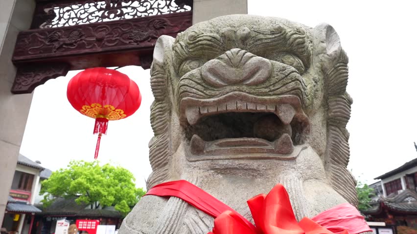 Close up of a stone lion sculpture beside Qibao main gate with a red lantern and pagoda visible in the background. Shanghai, China