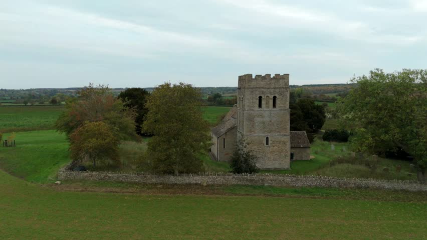 Aerial view of a stone church with a prominent square tower surrounded by green fields and trees, creating a serene rural scene, Stamford, England, United Kingdom.