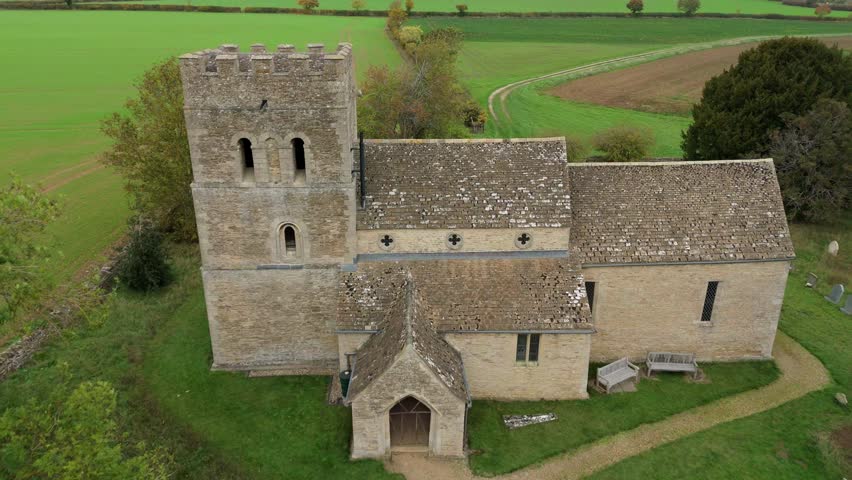 Aerial view of a stone church nestled among vibrant green trees and fields, contrasting with the muted tones of the building, Stamford, England, United Kingdom.