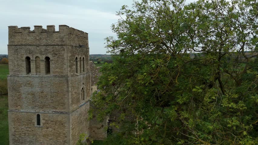 Aerial view of a stone church tower rising amidst green fields and trees, a picturesque landscape with a cloudy sky, Stamford, England, United Kingdom.