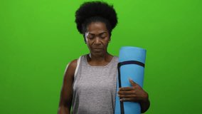 Woman holding blue yoga mat looking stressed against isolated green background with afro hairstyle, wearing sleeveless top, embodying calm and mindfulness. - Powered by Shutterstock - Get 15% off with code: PIKWIZARD15
