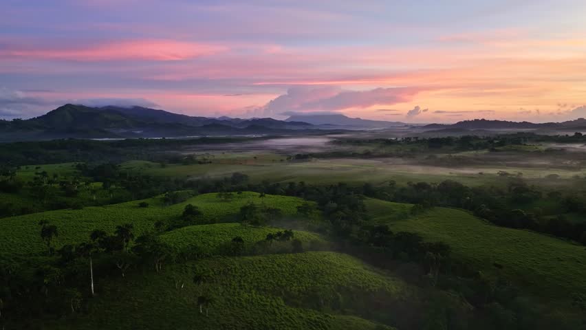 Rolling mountains and misty valleys against the backdrop of sunrise. Pink-orange clouds. Dawn mist in the early morning mountains. A natural landscape with a serene glow. A beautiful sunset.