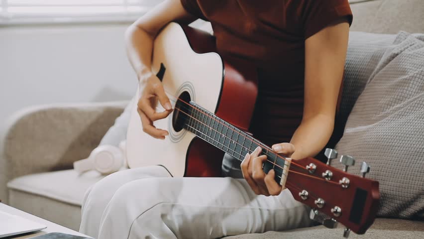 Young woman playing acoustic guitar and wearing headphones at home