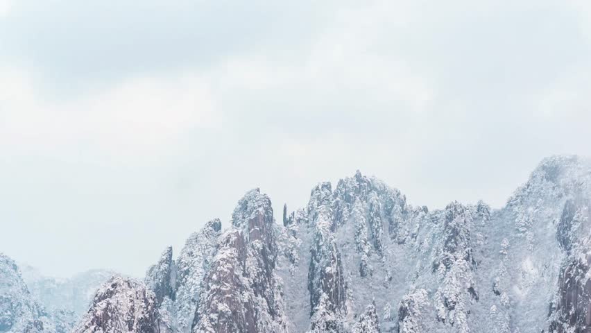 Snow covered mountain peaks against a cloudy sky on a cold winter day outdoors