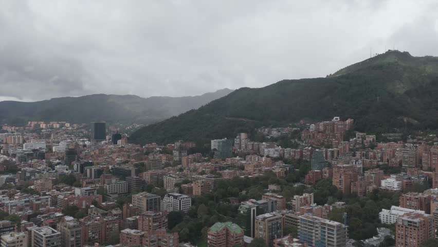 Bogota, Colombia – May 31, 2025: Drone aerial view of Bogota city showing urban buildings, green hills, and cloudy mountain landscape over the capital of Colombia.