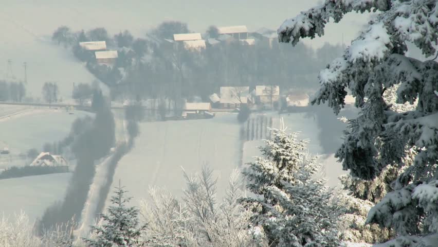 Snowy winter landscape with trees and houses covered in snow on a cold day