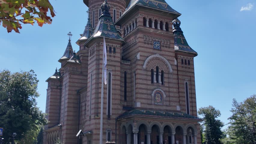 Scenic view of Timisoara’s Metropolitan Cathedral with natural foliage in the foreground, adding depth and charm to the landmark.