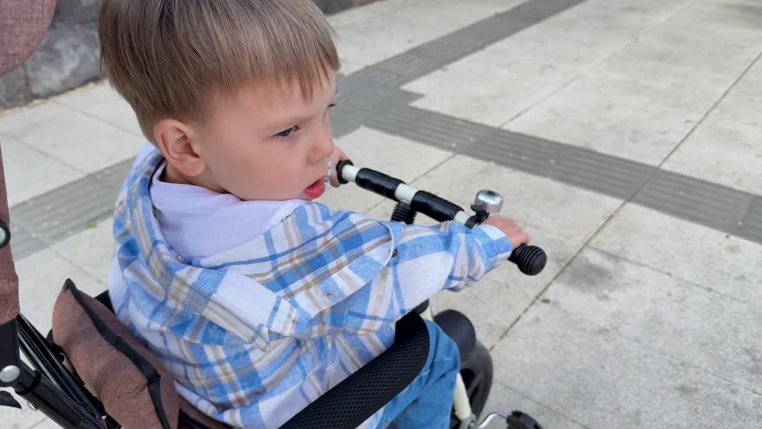 A happy child and his mother ride a tricycle in a park in summer along an alley.