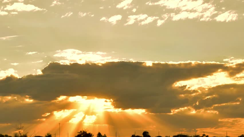Golden sunset with sun rays shining through clouds over a silhouetted landscape