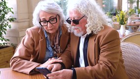 Happy senior couple sitting together at outdoor cafe using smartphone and looking at social media. Elderly people enjoying technology, connection, communication, digital lifestyle, love and leisure - Powered by Shutterstock - Get 15% off with code: PIKWIZARD15