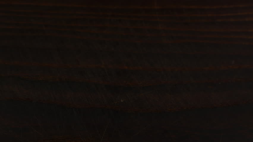 White sugar crystals are sprinkled onto a dark brown wooden surface. A big pile of sugar, a lot of sugar. Slow motion.