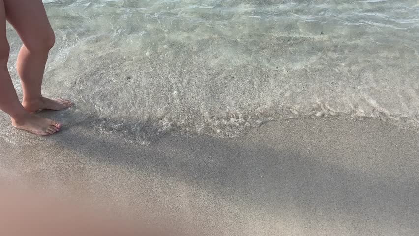 close up of feet walking through shallow transparent sea water at cala ses covetes beach mallorca spain
