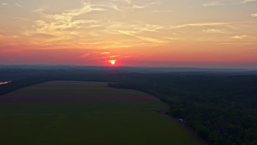 Aerial shot of the Potomac River at sunset. The calm water reflects the orange sky as the sun sets over distant mountains. Features agricultural fields near Poolesville, MD, and the Virginia shoreline