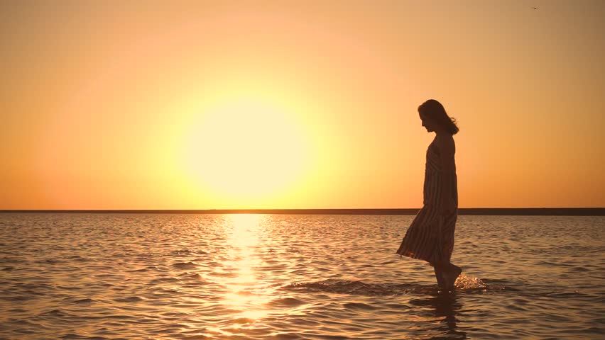 Young woman walks through shallow water at the beach during sunset
