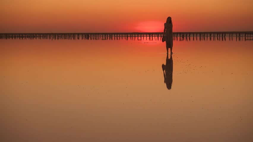 Young woman walks through shallow water at the beach during sunset
