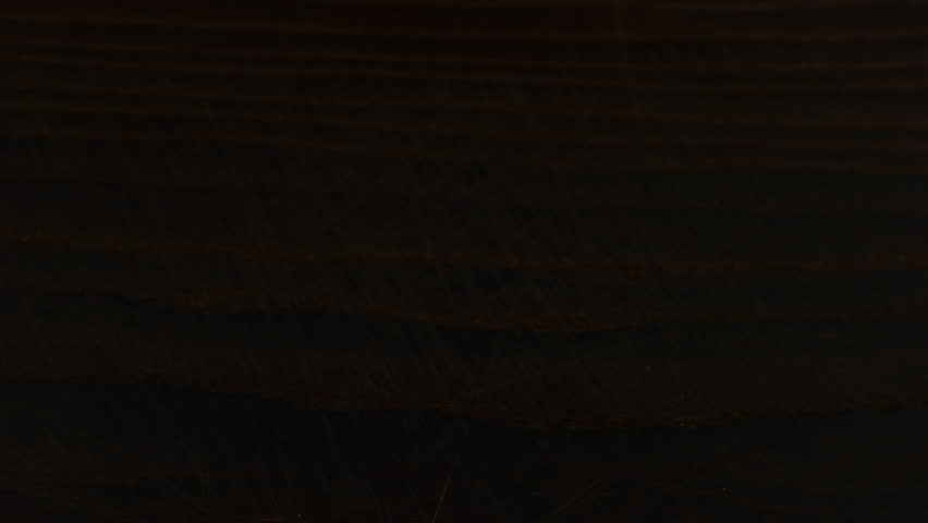 White sugar crystals are sprinkled onto a dark brown wooden surface. A big pile of sugar, a lot of sugar.