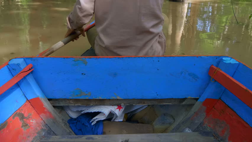 A fisherman rows his colorful boat through the mangroves of Tahas river while sitting on a bow of his boat. Near Kampong Phluk floating village, Cambodia