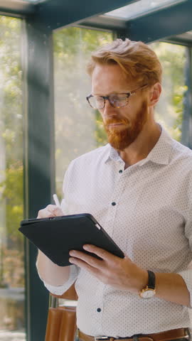 Caucasian architect in official clothes standing in middle of trendy studio with digital tablet and signing e-contract about cooperation with client. Expert working on creative space planning.
