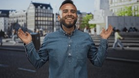 Man smiling with face and hands raised on a busy city street near stone steps and a monument, wearing a denim shirt and rings; joy. - Powered by Shutterstock - Get 15% off with code: PIKWIZARD15