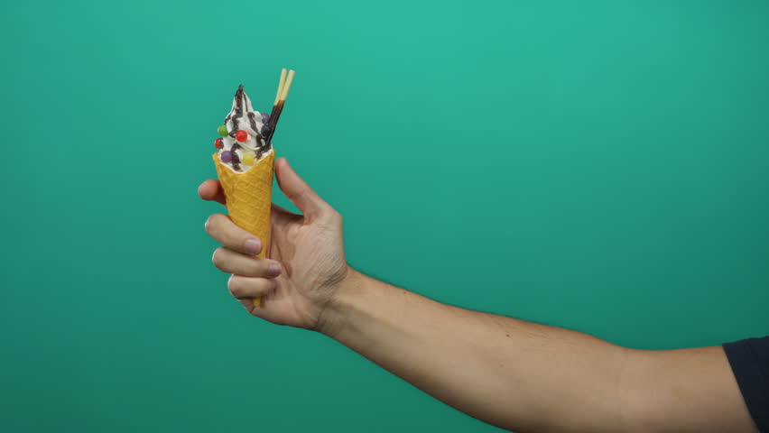 Man holding ice cream cone with toppings against green isolated background showcasing dessert indulgence.
