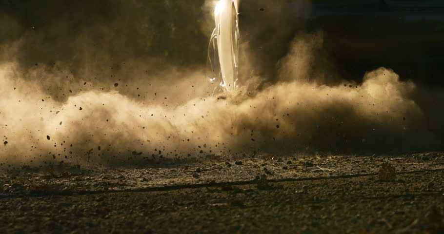 Slow motion close up of car wheel accelerating on gravel terrain, lifting dust and debris at 1000 fps.. Perfect for concepts of adventure, energy, and motion.