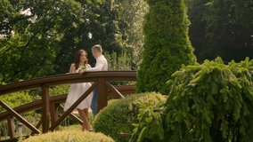 Romantic couple stands on a wooden bridge amidst lush green garden park foliage, sharing an intimate moment. The setting portrays romance and tranquility in nature 4K UHD B-Roll footage - Powered by Shutterstock - Get 15% off with code: PIKWIZARD15