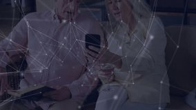 Mature woman tilting smartphone toward man in tech, sharing data while overlay drifting on sofa. Interconnection, companionship, retirement, digital lifestyle, relaxed, modern, communication - Powered by Shutterstock - Get 15% off with code: PIKWIZARD15