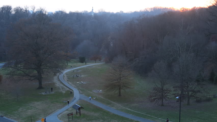 People walk on the exercise trail in Rock Creek Park at winter dusk south of the Taft Bridge, with Rock Creek Parkway traffic in the background.