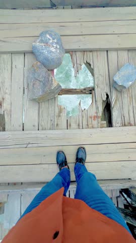 Boy looking down a hole in a rustic wooden bridge at the raging turquoise river below 