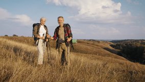 Smiling old man and woman travellers stand on hill slope at autumn countryside. Mature family engages in Nordic walking in nature park against blue sky - Powered by Shutterstock - Get 15% off with code: PIKWIZARD15