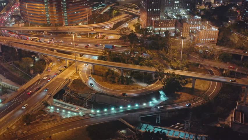 Nighttime aerial view of a bustling urban highway interchange with illuminated roads, flowing traffic, and a vibrant city skyline against the dark sky. - Powered by Shutterstock - Get 15% off with code: PIKWIZARD15