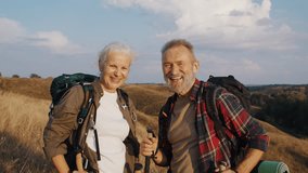 Smiling elderly pair rests on hill top after Nordic walking ascent. Senior woman lifts pole and mature man smiles nodding head while looking at golden sunset - Powered by Shutterstock - Get 15% off with code: PIKWIZARD15