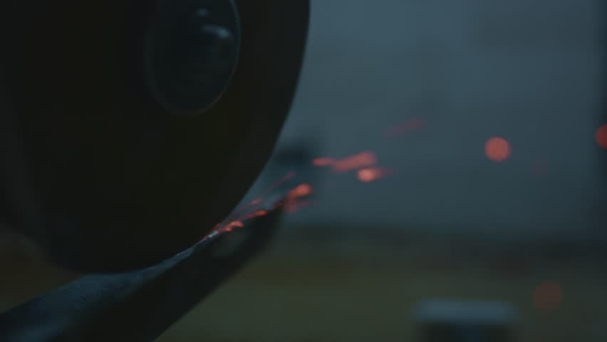 An angle grinder sharpens a steel impact tool. Sparks fly from the power tool blade. Close-up of spinning disc in motion, creating dynamic shower of fire. Angle grinder machine cutting iron in factory