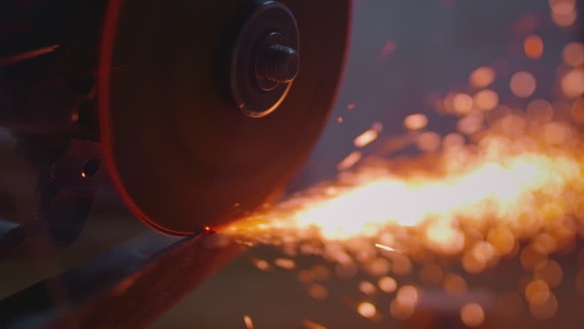 An angle grinder sharpens a steel impact tool. Sparks fly from the power tool blade. Close-up of spinning disc in motion, creating dynamic shower of fire. Angle grinder machine cutting iron in factory