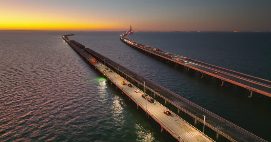 Fishing pier and highway road traffic driving at Sunshine Skyway Bridge in Florida at sunset. Transportation infrastructure in USA