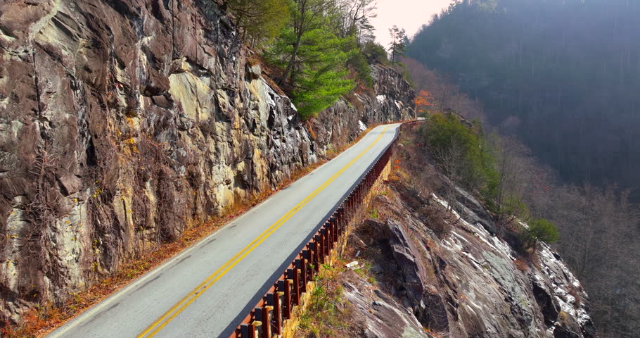 Highlands Road mountain highway in North Carolina during fall. Vehicle driving through forested hills and rocky ridgelines under colorful trees.