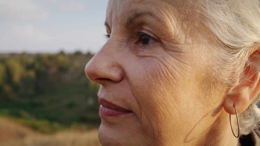 Senior woman face with closed eyes during mindfulness pause. Grey-haired woman breathes in and keeps calm smile standing still near trail after Nordic walking