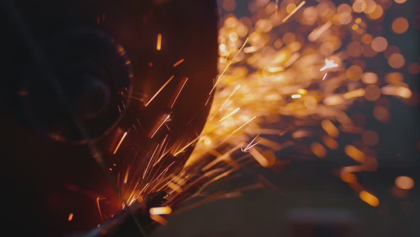Sparks fly from cutting metal with angle or electric grinder. Metal turning disc cuts the material. Detail shot of cutting iron with circular saw. Welder is working steel at industrial plant.